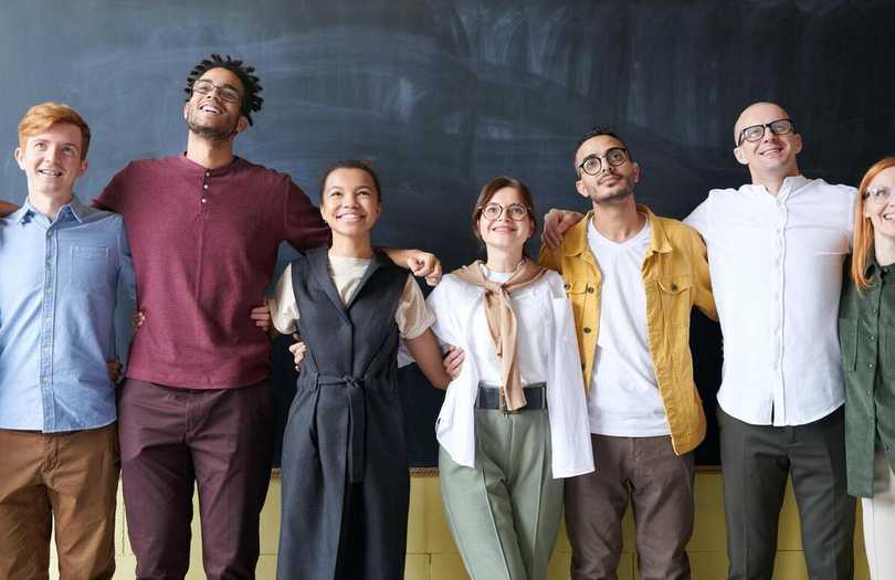 Illustration : équipe souriante et diversifiée et naturelle, se tenant par les épaules devant un tableau noir en souriant. Le numérique responsable peut être un levier de marque-employeur